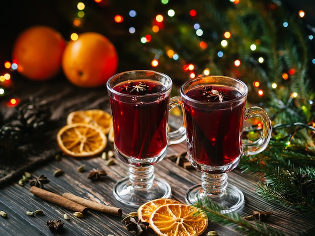 Vinho quente em copos na mesa decorada com uma árvore de natal. fatias de laranja, estrelas de anis, cardamomo, canela