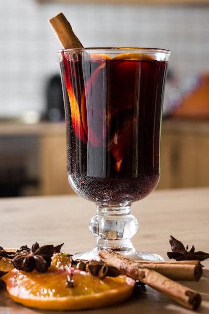 Foto vinho quente em vidro com especiarias e frutas na mesa de madeira.