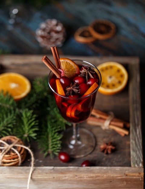 Vinho quente quente de Natal em um copo com especiarias, frutas cítricas e amora. Atmosfera de Natal.