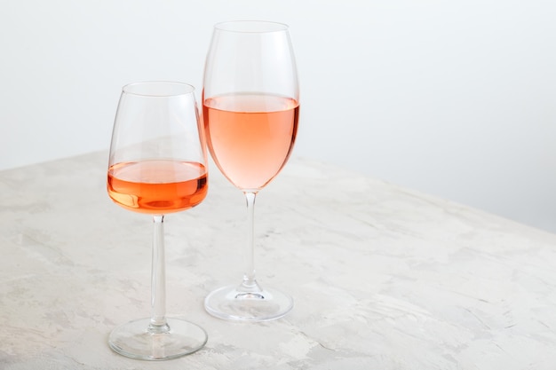 Vinho rosa em diferentes tipos de copos sobre fundo claro de concreto. composição mínima do vinho na mesa branca com espaço de cópia.