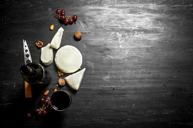 Vinho tinto com queijo de ovelha fresco e uvas. Em um fundo preto de madeira