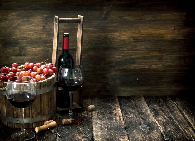 Vinho tinto com um balde de uvas na mesa de madeira.