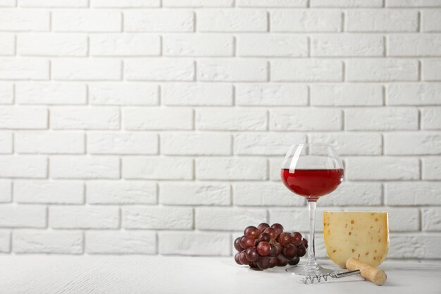 Vinho tinto com uva e queijo no fundo da parede de tijolos