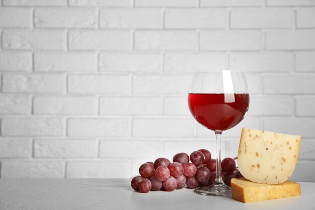 Vinho tinto com uva e queijo no fundo da parede de tijolos