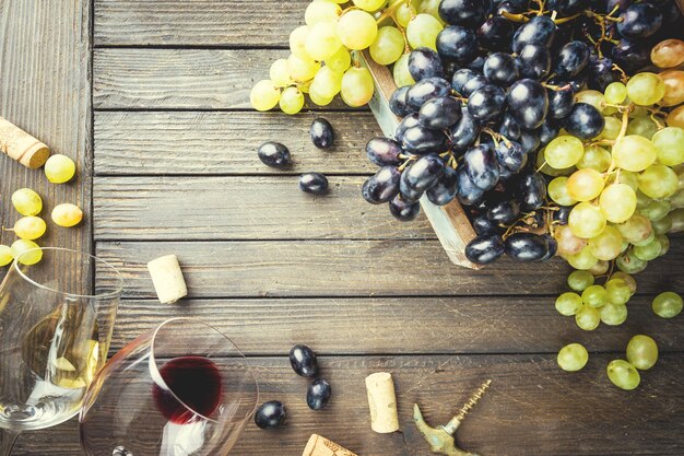 Vinho tinto e branco com taça, garrafa e uvas sobre madeira