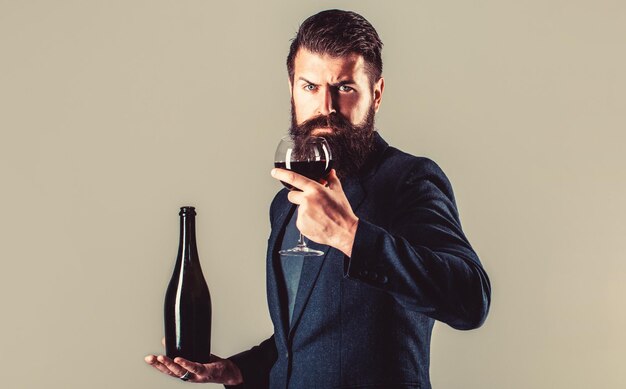 Vinho tinto em garrafa, copo de vinho. Vinho tinto em uma taça. Homem sommelier, degustador, vinícola. Garrafa, copo de vinho tinto. Homem de barba, barbudo, sommelier, degustador