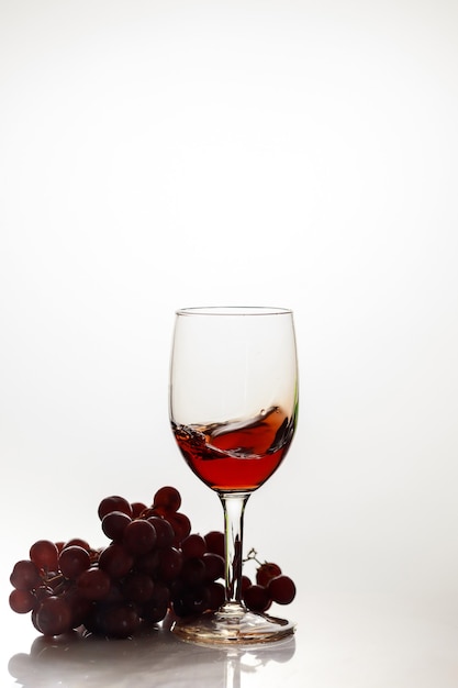 Vinho tinto em vidro com uva vermelha na superfície branca.