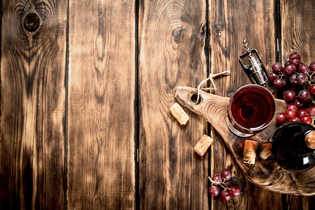 Vinho tinto na placa de madeira com rolhas e um saca-rolhas na mesa de madeira.