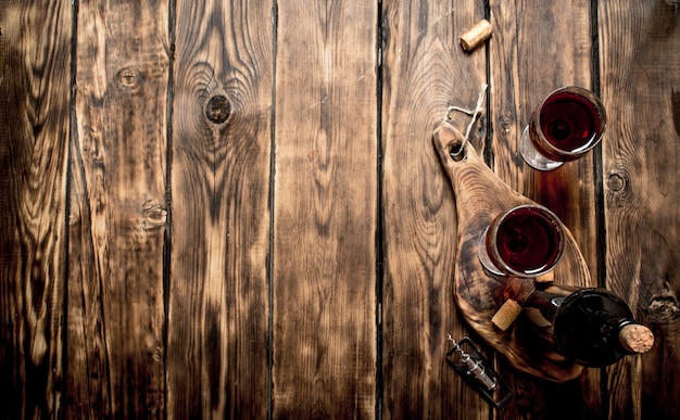 Vinho tinto na placa de madeira com rolhas e um saca-rolhas na mesa de madeira.