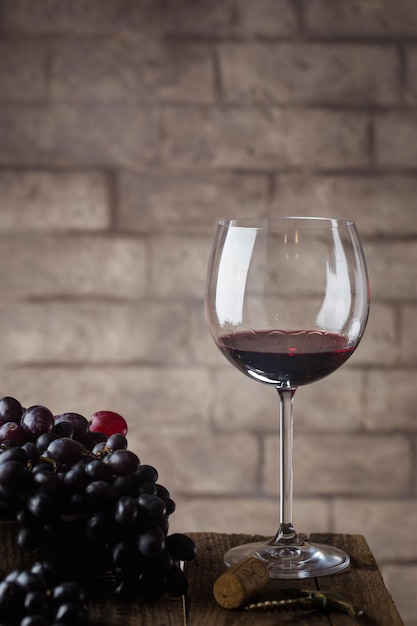 Vinho tinto na taça e uvas maduras na mesa de madeira