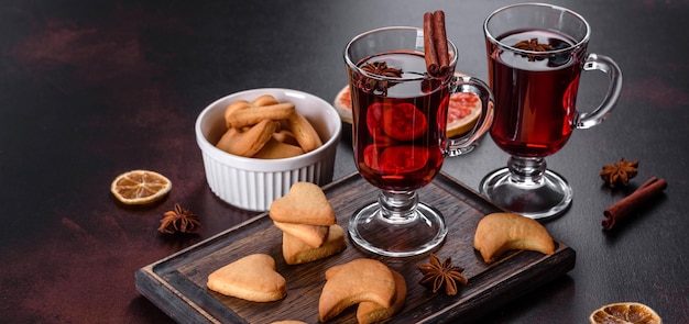 Vinho tinto quente com especiarias e frutas de Natal em uma mesa escura.