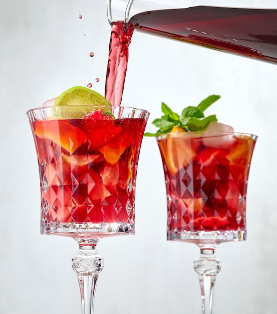 Vinho tinto servindo em um copo de frutas cortadas. processo de fazer sangria vermelha