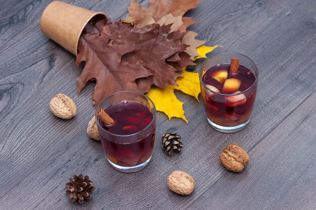 Vinho vermelho quente com especiarias e frutas em uma mesa de madeira. Folhas de outono outono.