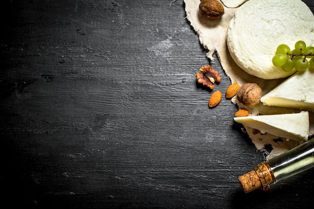 Vino blanco con queso de cabra, uvas y frutos secos. Sobre un fondo de madera negra