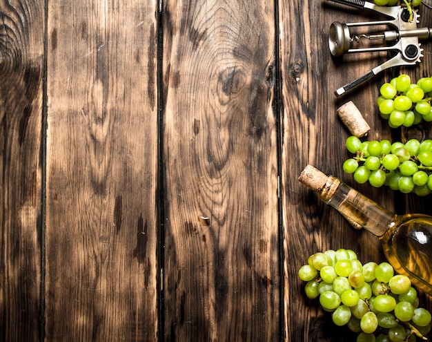 Vino blanco con sacacorchos y ramas de uva en una mesa de madera