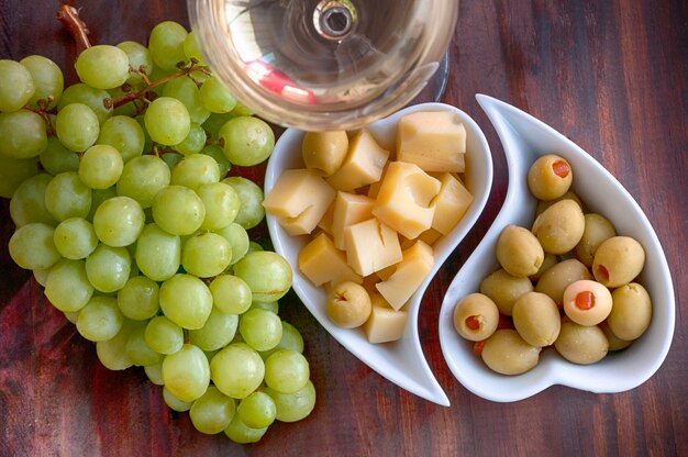 Vino blanco, uva, aceitunas y queso en la mesa de woden