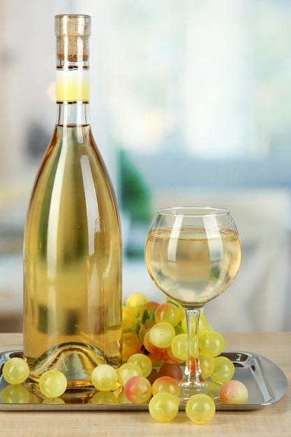 Vino blanco en vaso con botella en salver en el fondo de la habitación