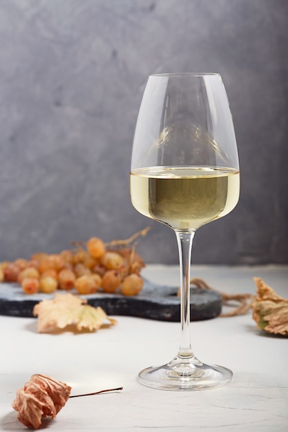 Vino blanco en un vaso y uvas sobre la mesa.