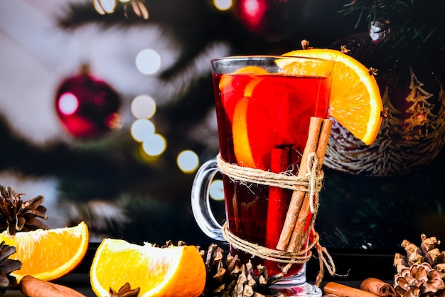 Foto vino caliente bebida caliente de navidad con especias sobre un fondo oscuro. rodajas de naranja, palitos de canela, conos de navidad, bokeh brillante. ambiente de vacaciones, estilo rústico. la idea de crear tarjetas de felicitación.