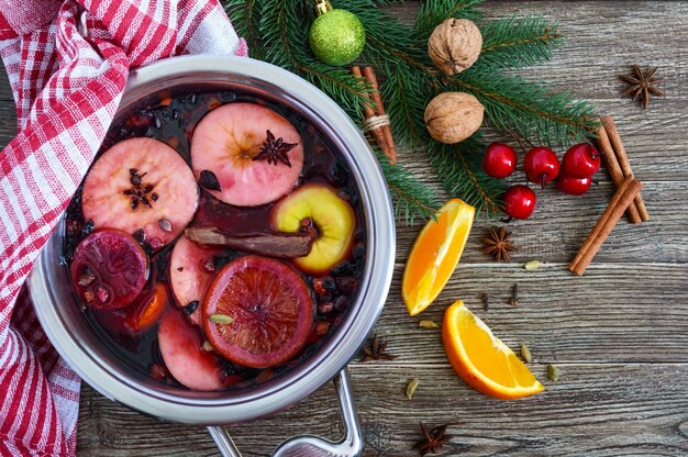 Vino caliente caliente en una sartén grande sobre una mesa de madera. Bebida tradicional de invierno aromática a base de vino, jugo, especias, condimentos, frutas. Vista superior.