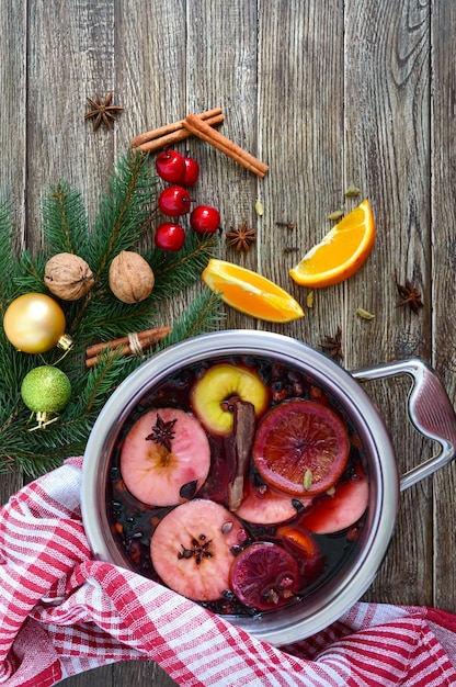 Vino caliente caliente en una sartén grande sobre una mesa de madera. Bebida tradicional de invierno aromática a base de vino, jugo, especias, condimentos, frutas. Vista superior.