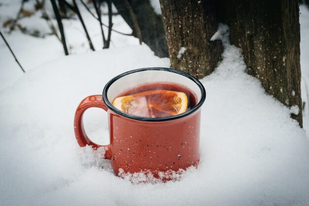 Vino caliente en copa tinto. Bebida caliente de invierno al aire libre en el bosque nevado de invierno en clima frío.