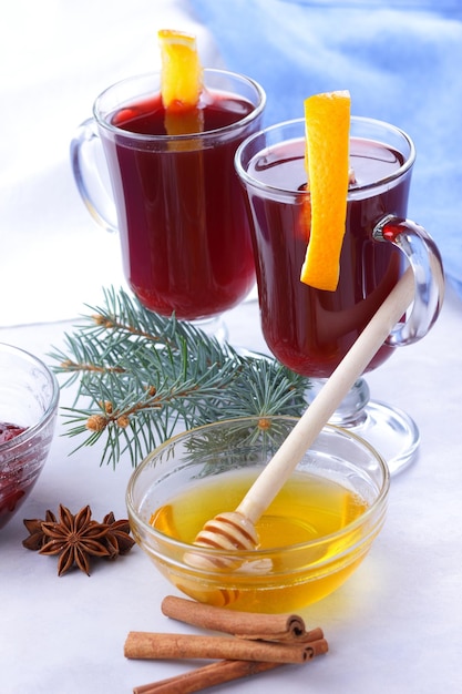 Vino caliente con especias de miel y rodajas de naranja sobre un fondo claro Delicioso vino caliente en un vaso con ramas de abeto y una servilleta azul