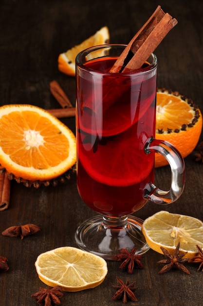 Vino caliente fragante en vidrio con especias y naranjas alrededor de la mesa de madera