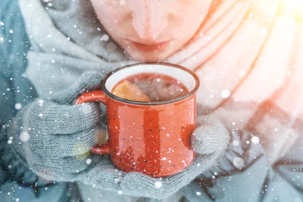 Vino caliente en manos de una niña durante una nevada en el bosque con bebidas calientes de invierno aromáticas