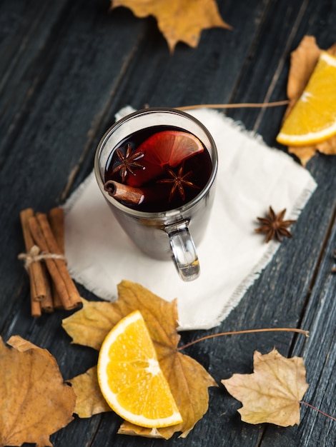 Vino caliente en una mesa de madera oscura con canela, anís y hojas secas de otoño