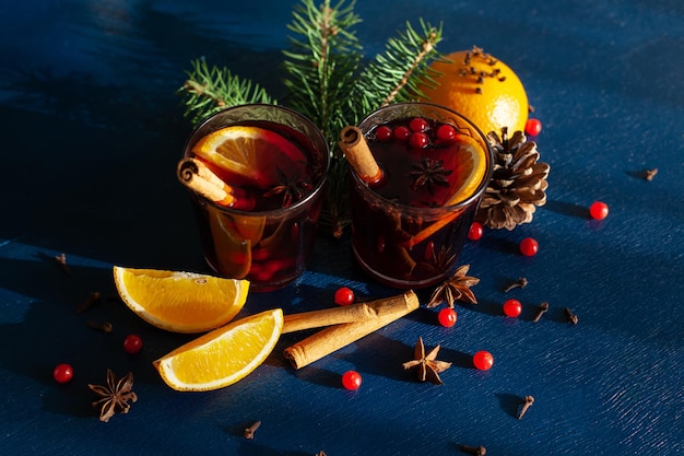 Vino caliente de Navidad con canela, naranja, anís y clavo con sombras de la luz del sol sobre un fondo azul. Vacaciones de invierno.