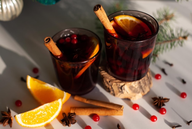 Vino caliente de Navidad con canela, naranja, anís y clavo con sombras de la luz del sol sobre un fondo blanco. Vacaciones de invierno.