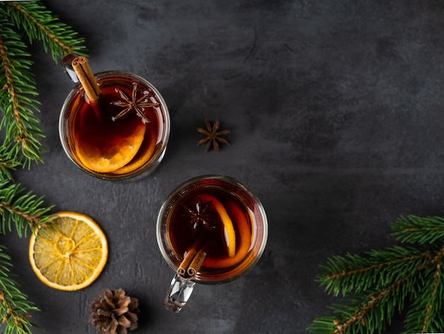 Vino caliente con rodajas de naranja, estrellas de anís, especias y palitos de canela sobre fondo oscuro con ramas de spruse. Navidad y año nuevo diseño plano. Vista superior de bebidas.