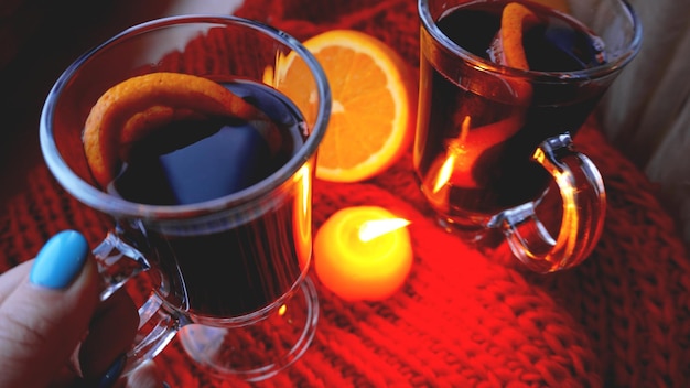 Vino caliente en tazas de vidrio velas encendidas sobre un fondo rojo oscuro Vino rojo caliente con bufanda naranja y roja