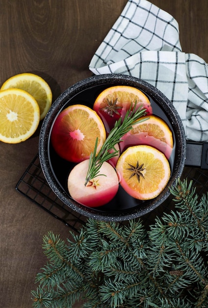 Vino caliente con trozos de naranja y manzanas en un cucharón negro sobre un fondo de madera