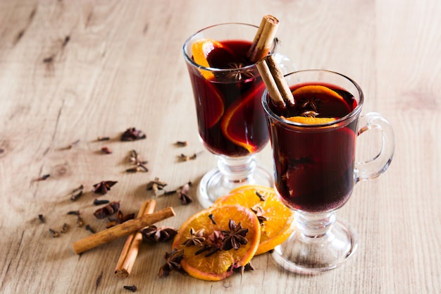 Vino caliente en vidrio con especias y frutas en la mesa de madera.