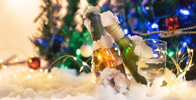 Vino de celebración navideña y copa de vino en la nieve y árbol de Navidad en un fondo borroso.