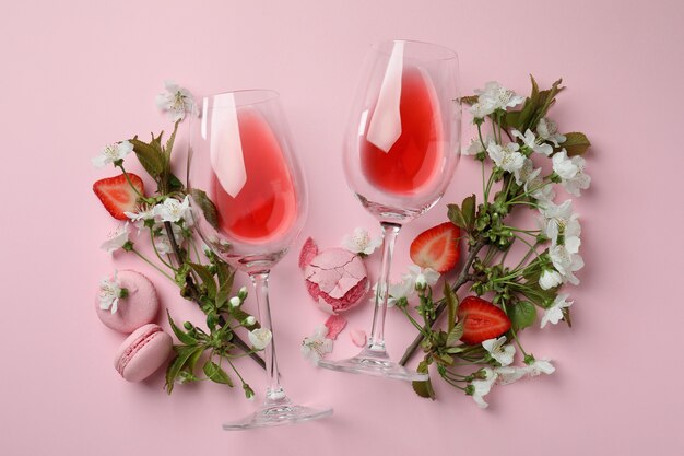 Vino, macarrones, fresa y flores sobre fondo rosa