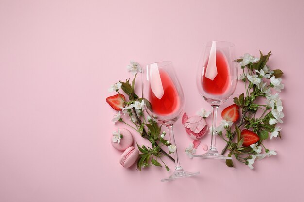 Vino, macarrones, fresa y flores sobre fondo rosa