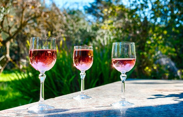 Vino rosado en copas de tallo sobre una mesa en un jardín.