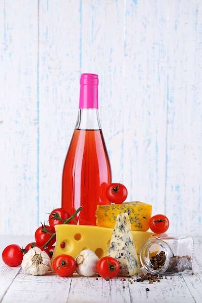 Vino rosado y diferentes tipos de queso sobre fondo de madera