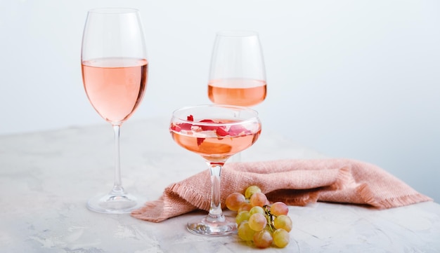 Vino rosado en diferentes tipos de vasos sobre fondo de hormigón claro con uvas composición de vino en ...