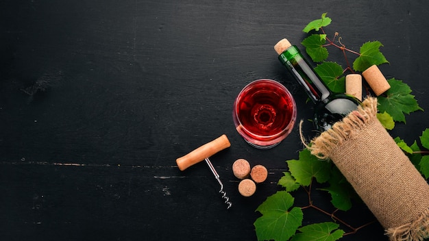 Vino tinto en una botella con un vaso y uvas Sobre un fondo de madera negra Espacio libre para texto Vista superior