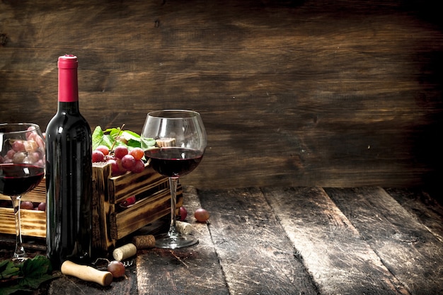 Vino tinto con una caja de uvas en la mesa de madera.