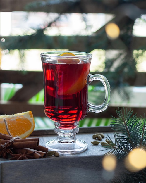 Vino tinto caliente de Navidad con especias y frutas sobre fondo decorado de Navidad