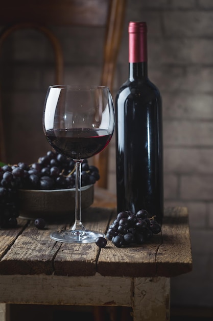 Foto vino tinto en un vaso y uvas maduras sobre mesa de madera