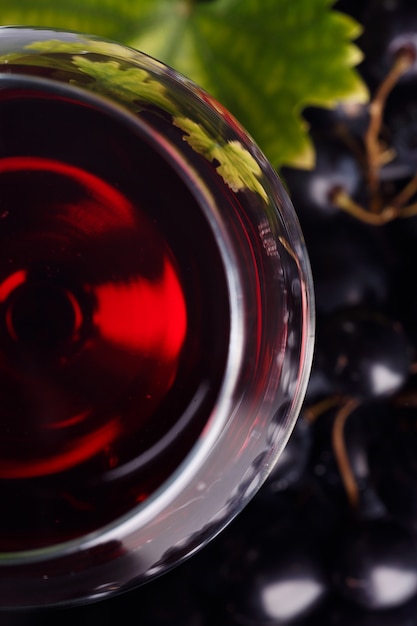 Vino tinto en un vaso y uvas sobre la mesa.