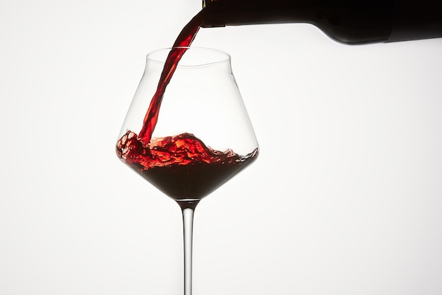 El vino tinto se vierte de la botella en un vaso transparente.