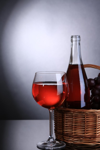 Vino de uvas maduras y botella de vino sobre un fondo gris