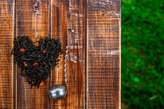 Vintage colador cerca de hojas secas de té negro en corazón sobre mesa de madera